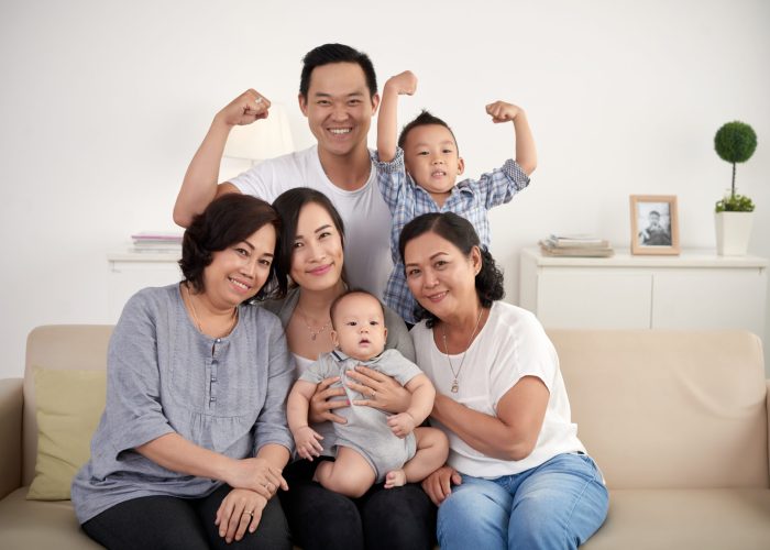Portrait of big Asian family posing for photo at home: sitting on sofa, looking at camera and smiling happily